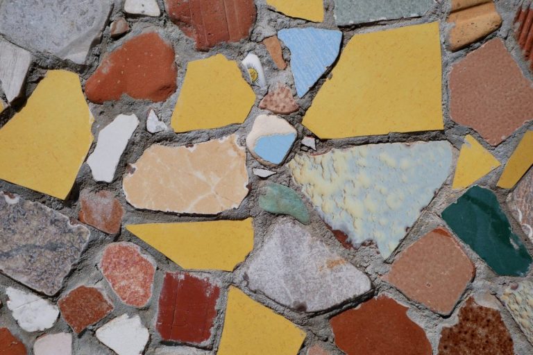 Vibrant mosaic of broken tiles in various colors and shapes, forming a textured wall pattern.